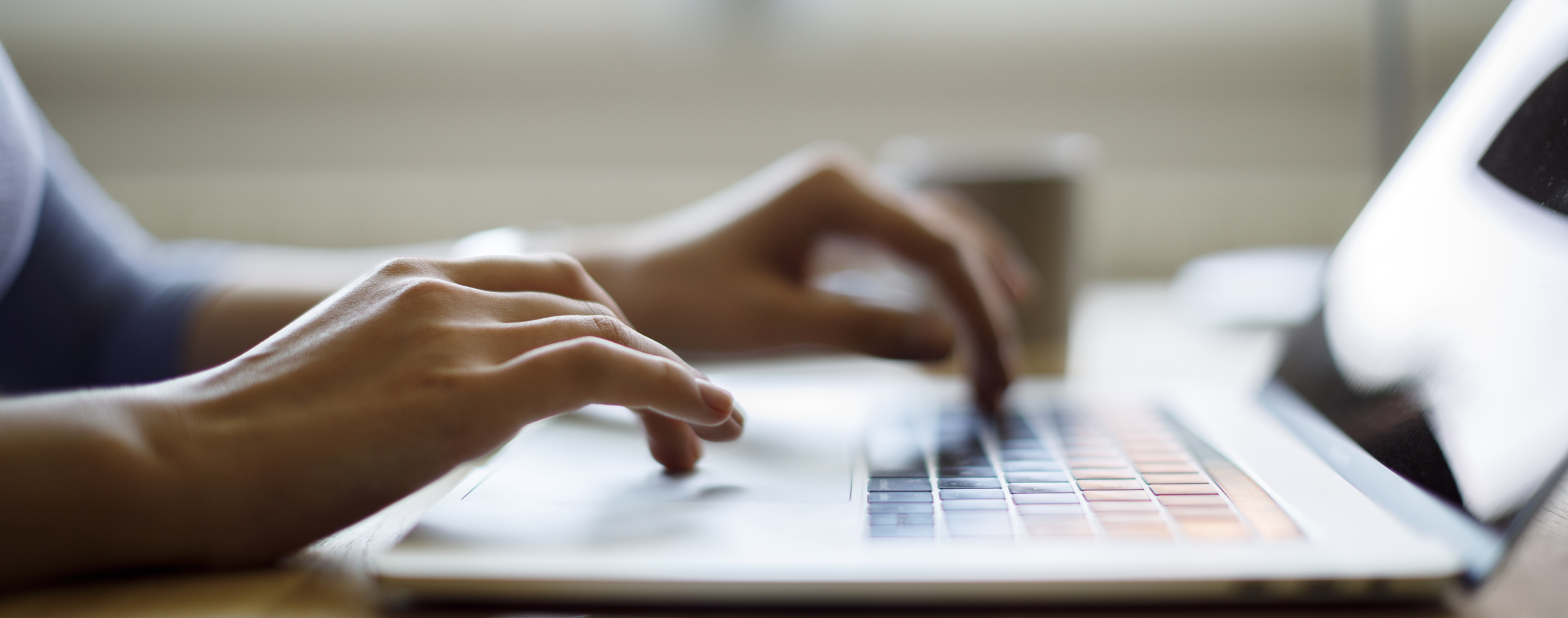 Image of person typing on laptop with hands in focus and the background and laptop blurred
